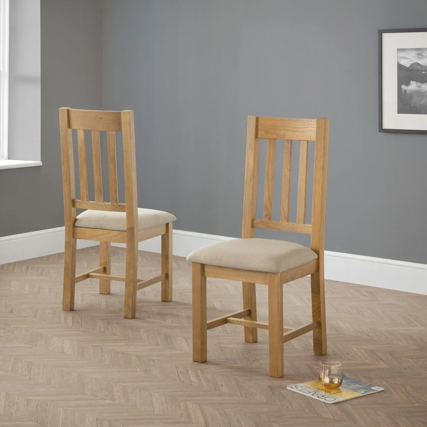 Pair of oak dining chairs with beige upholstered seats on wooden floor in modern room