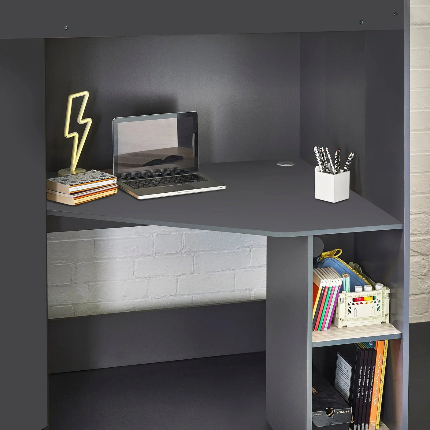 Grey corner desk with laptop, stationery holder and books on open lower shelves