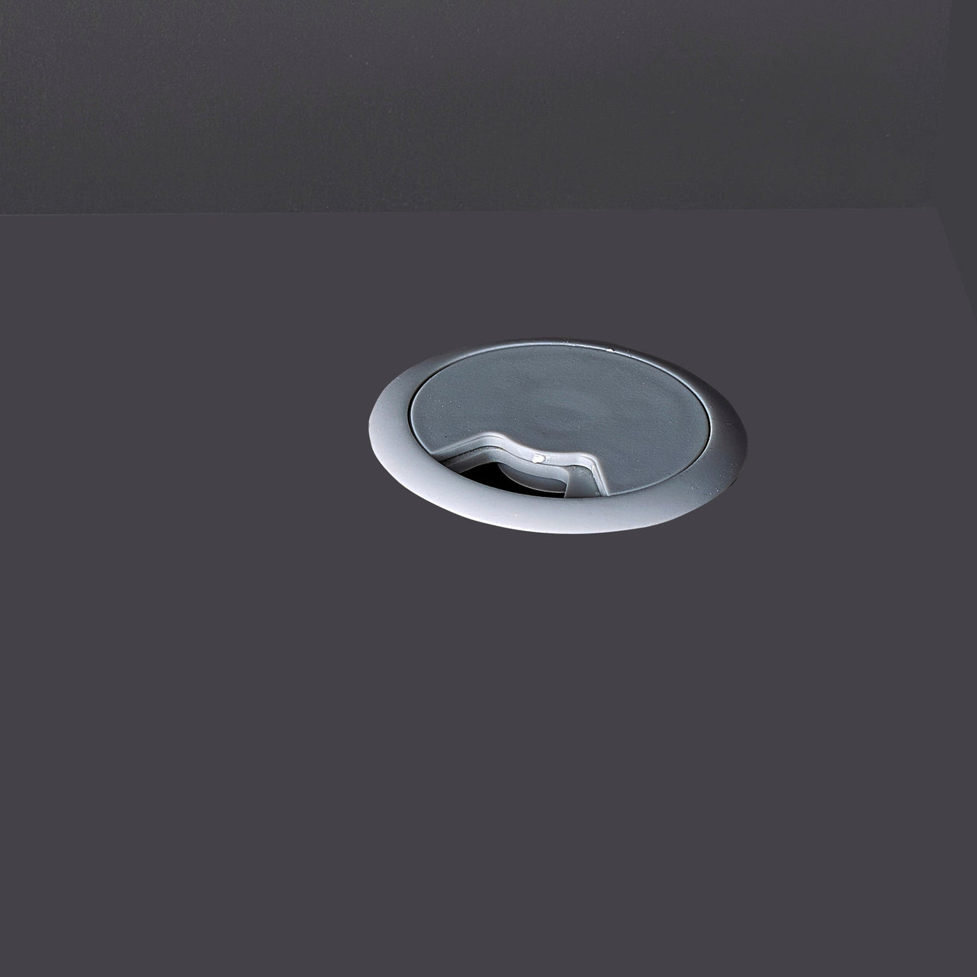 Silver cable management grommet fitted into dark wood office desk surface