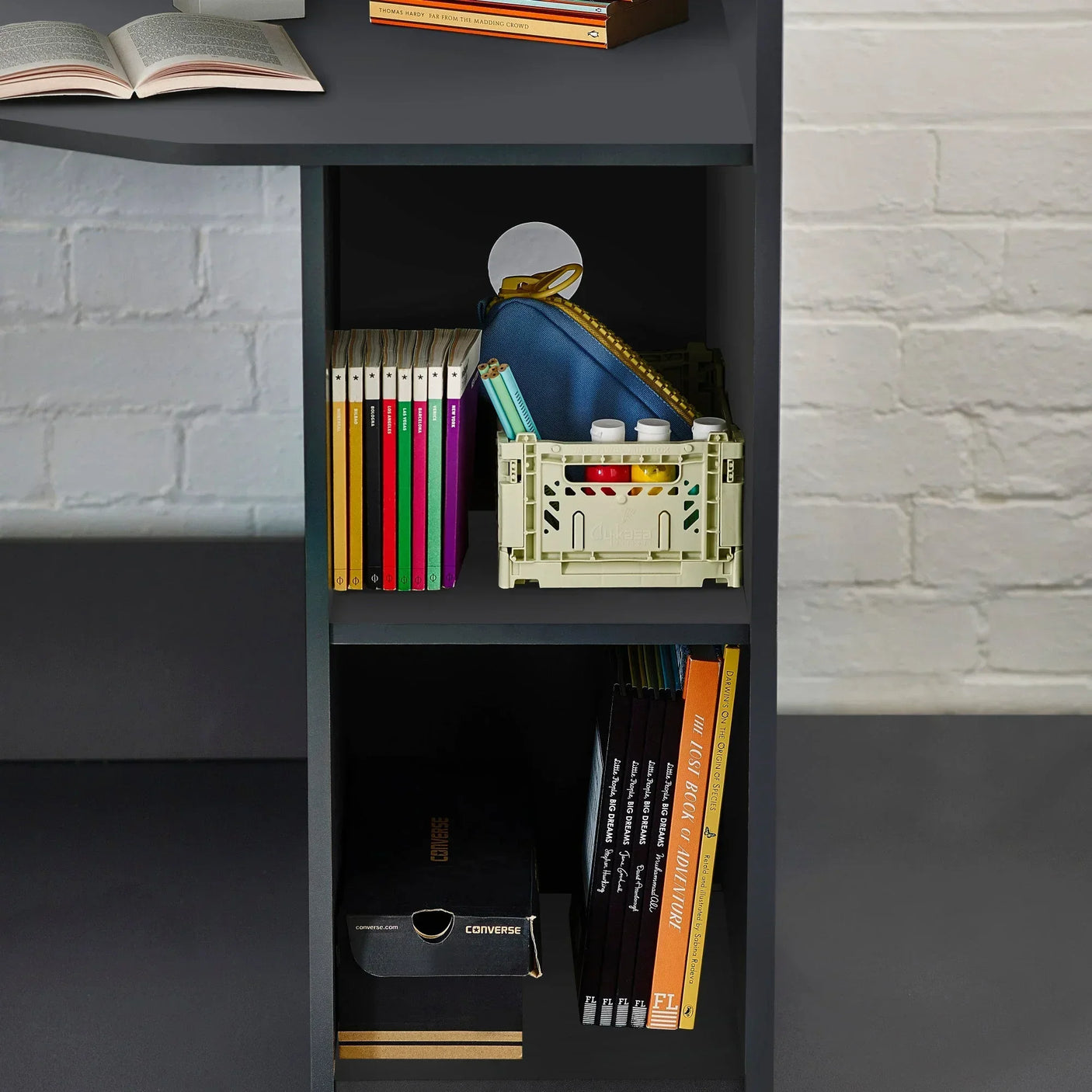 Black desk with bookshelf storage displaying books, crate, and pencil case