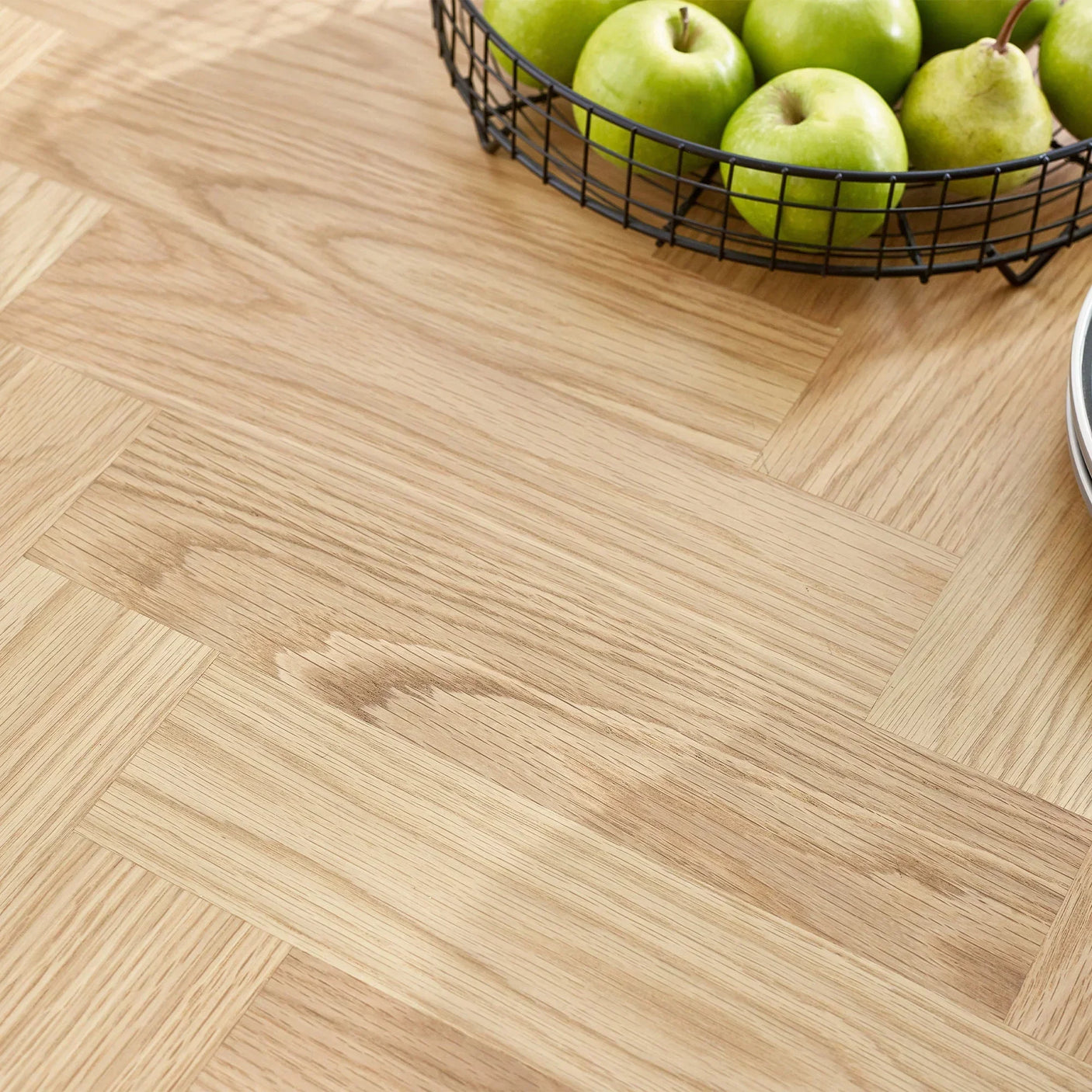 Oak dining table surface with herringbone pattern and basket of green apples