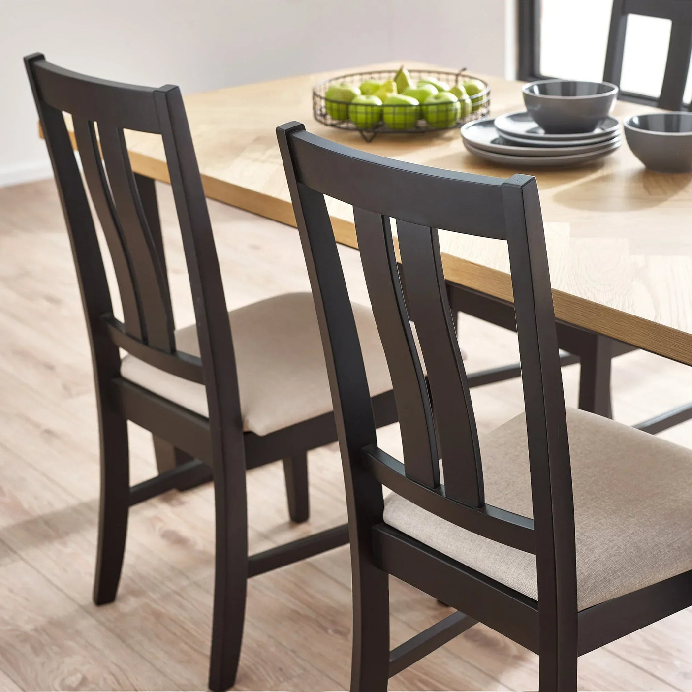 Black wood dining chairs with upholstered seats next to oak dining table, place settings visible