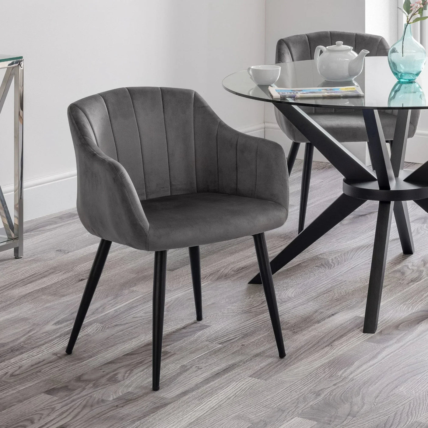 Grey velvet dining chair with black legs beside round glass dining table