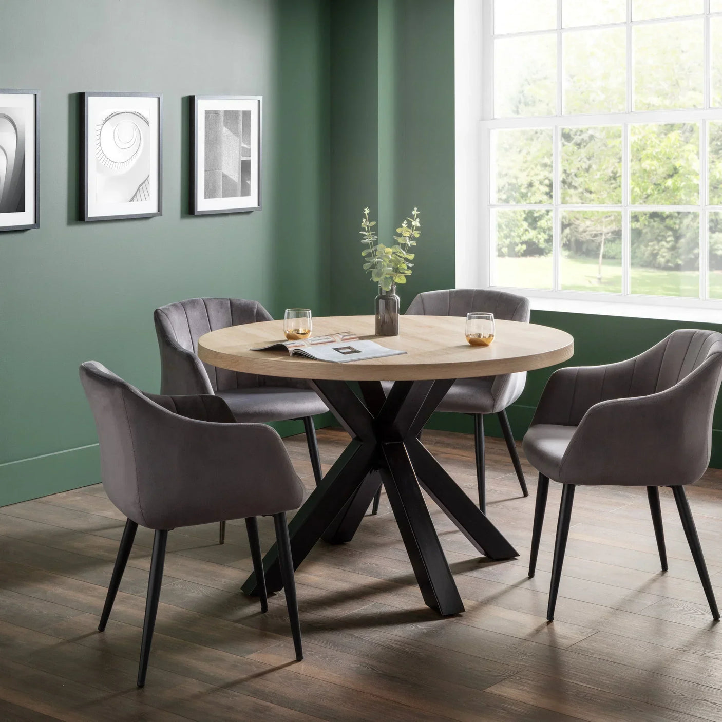 Round wooden dining table with black metal legs and four grey upholstered chairs in modern room