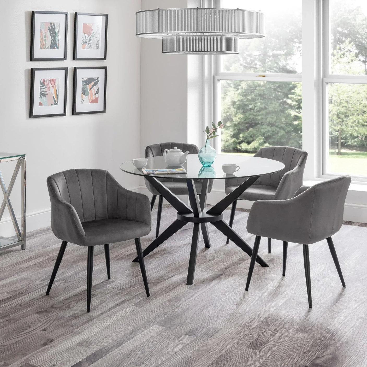 Glass dining table with black legs and four grey velvet chairs in modern dining room