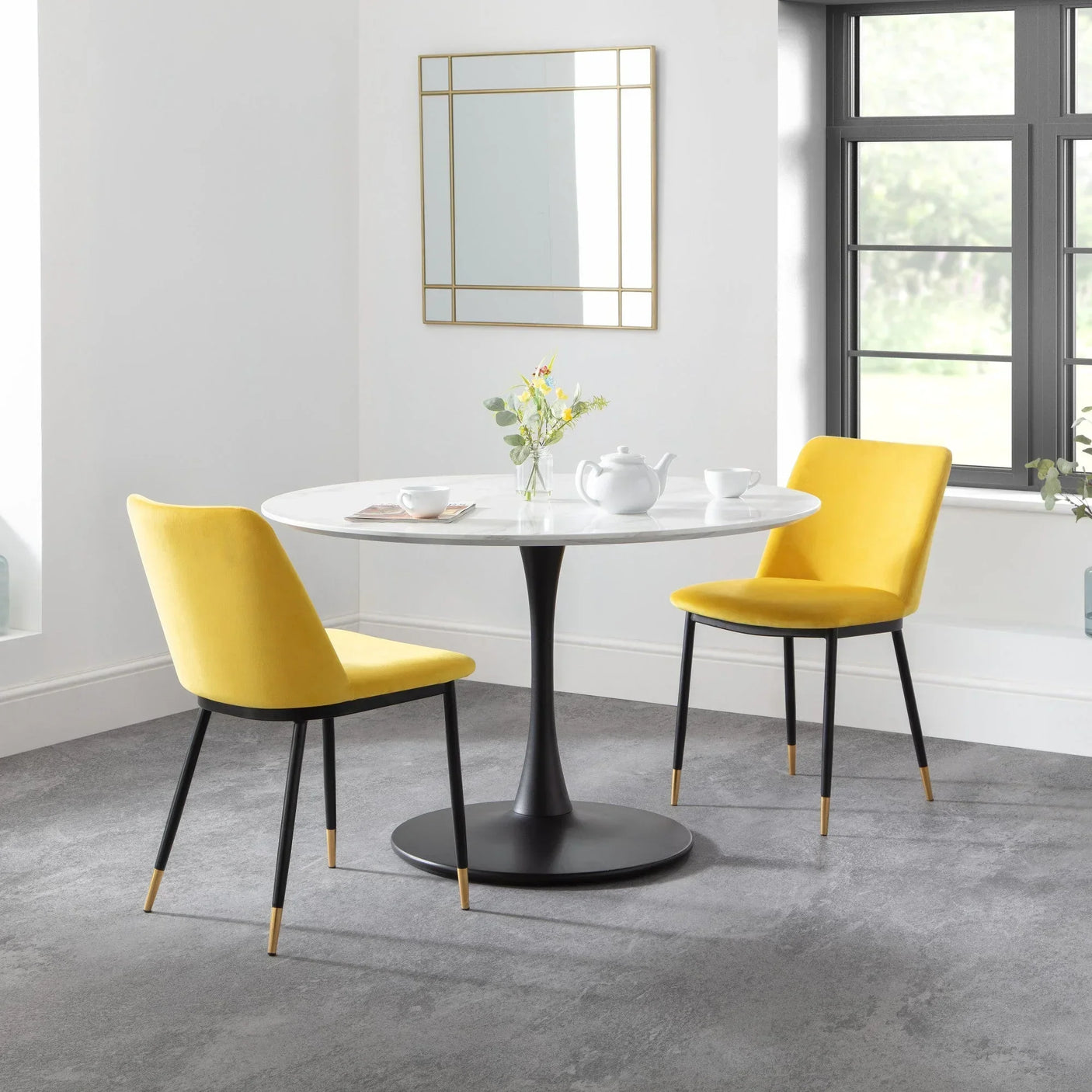 Round white dining table with black pedestal base and two yellow velvet chairs in modern room