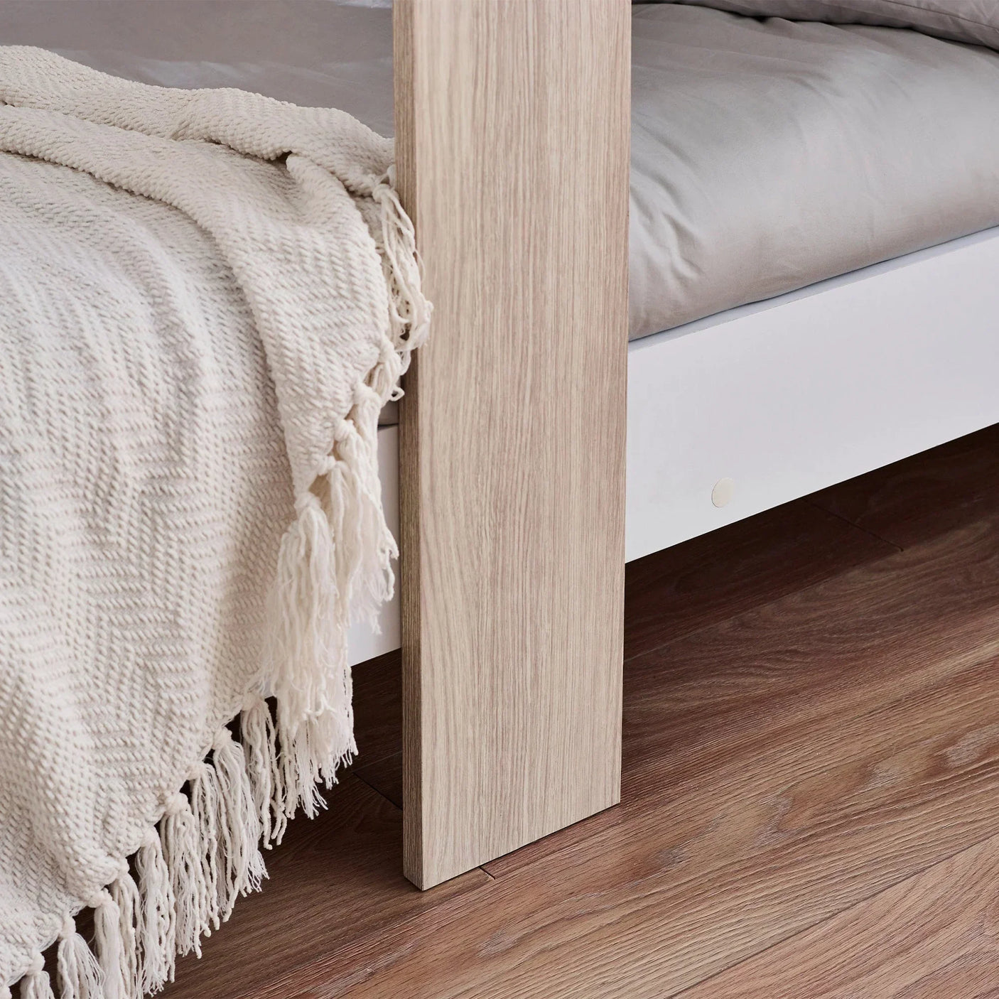 Pale wood bunk bed corner detail with white frame and textured cream blanket