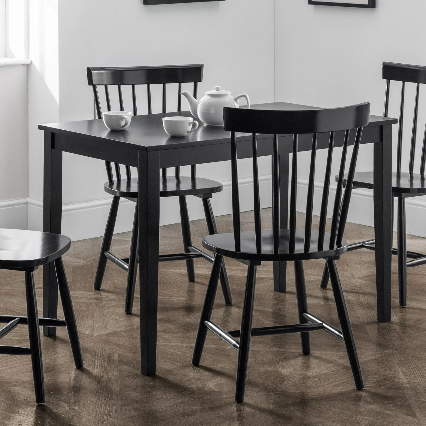 Black dining table with matching wooden chairs set on parquet floor in bright room