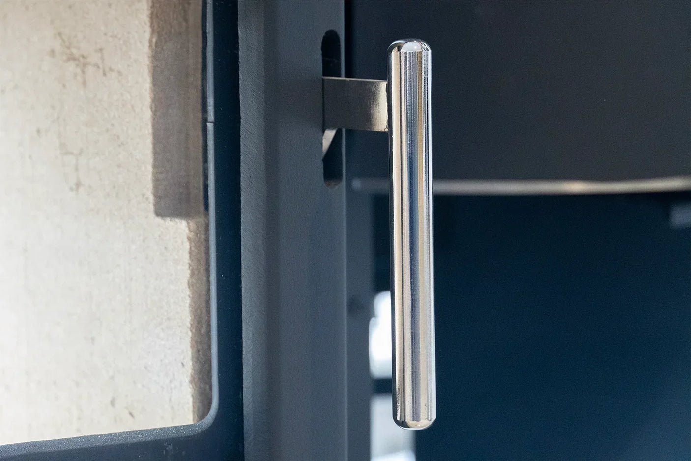 Stainless steel stove handle attached to black door, close-up on modern hardware detail