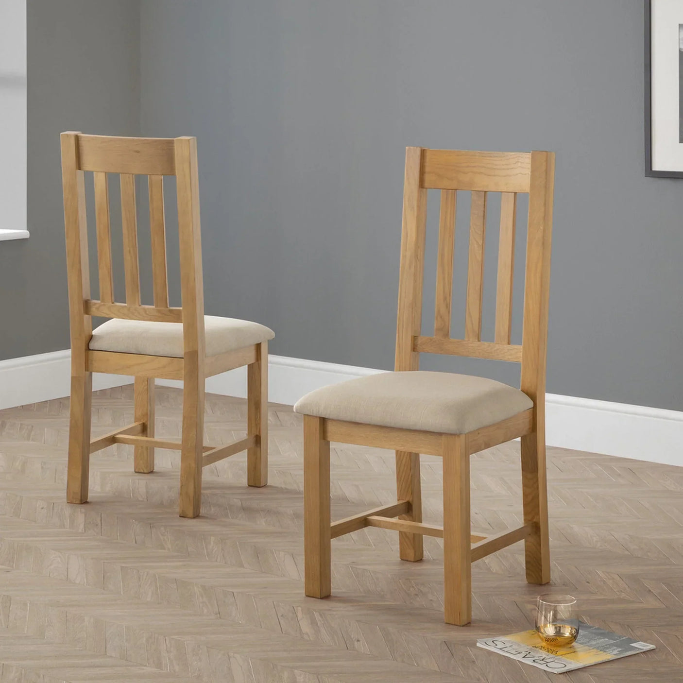 Pair of oak dining chairs with slatted backs and beige cushions in modern room