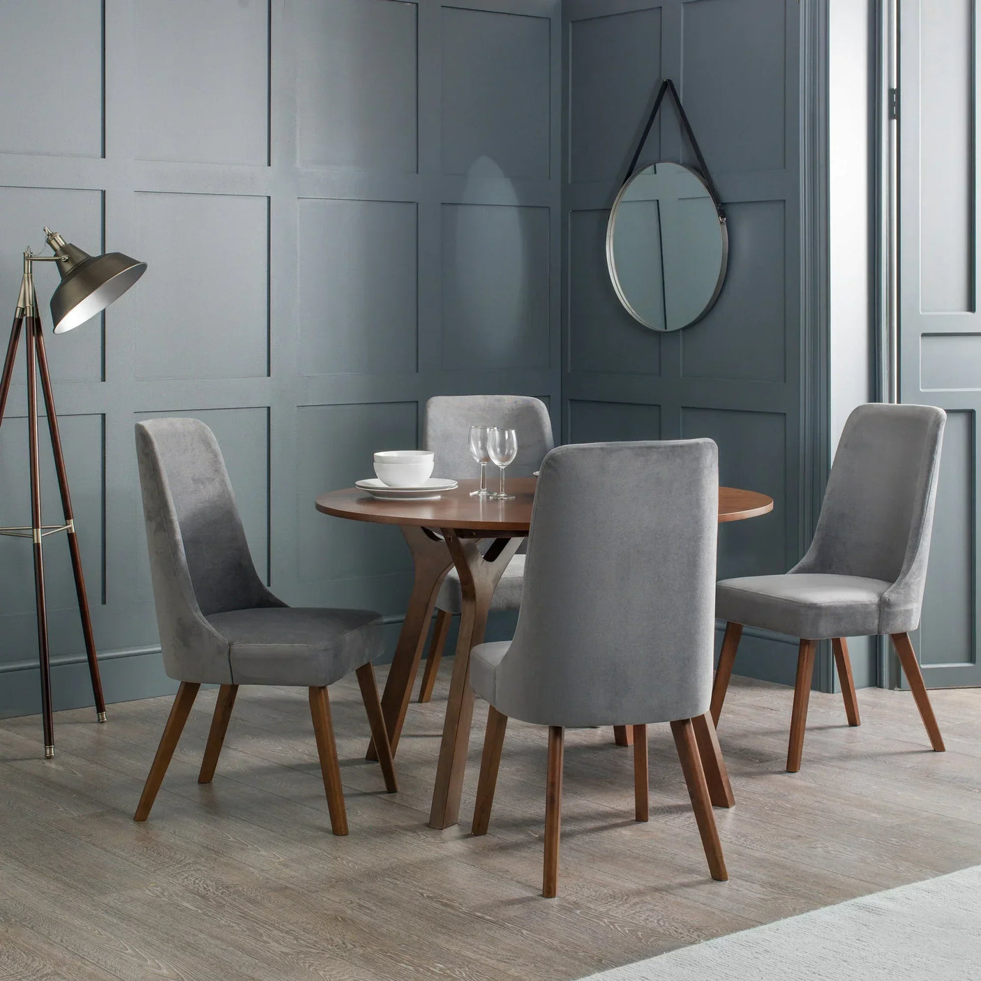 Round wooden dining table with four grey velvet chairs in modern dining room