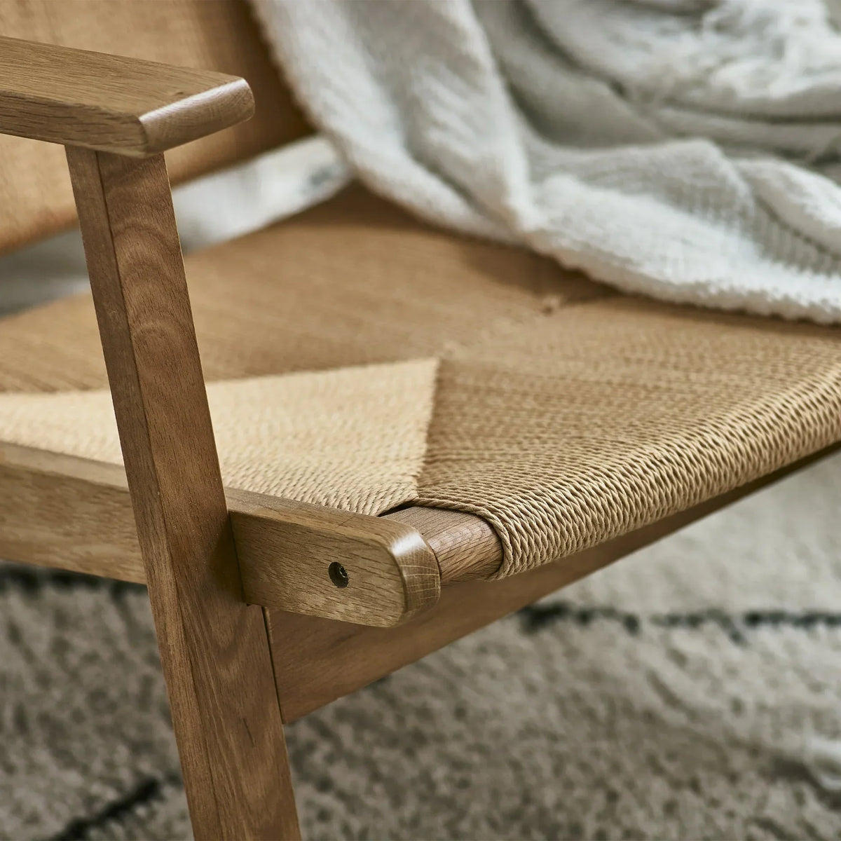 Close-up of woven lounge chair seat with oak wood armrest and light throw blanket