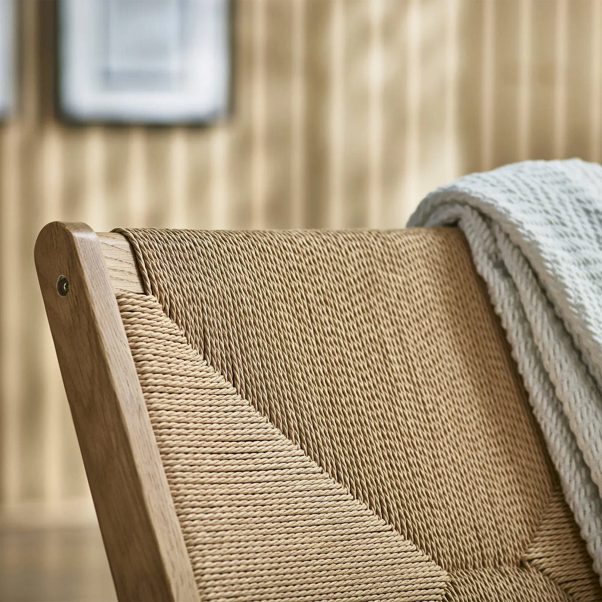 Close up of woven rope lounge chair backrest with natural wood frame and draped throw