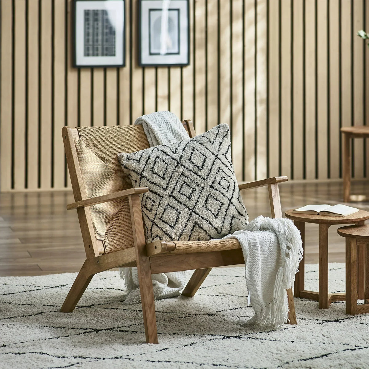 Wooden armchair with woven seat, patterned cushion and throw, next to small side tables