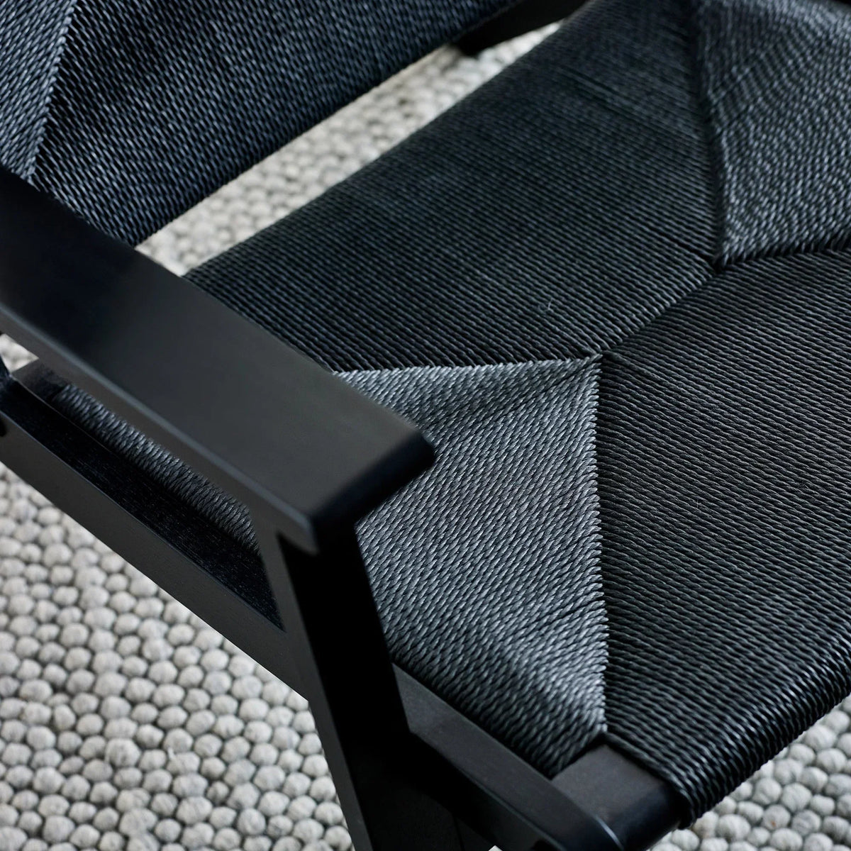 Close-up of woven black dining chair seat with wooden frame on textured rug