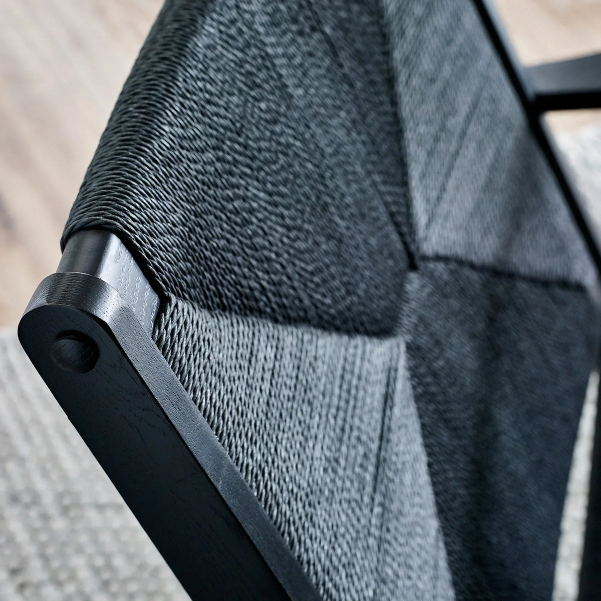 Close-up of black woven chair seat with wooden frame and textured geometric pattern