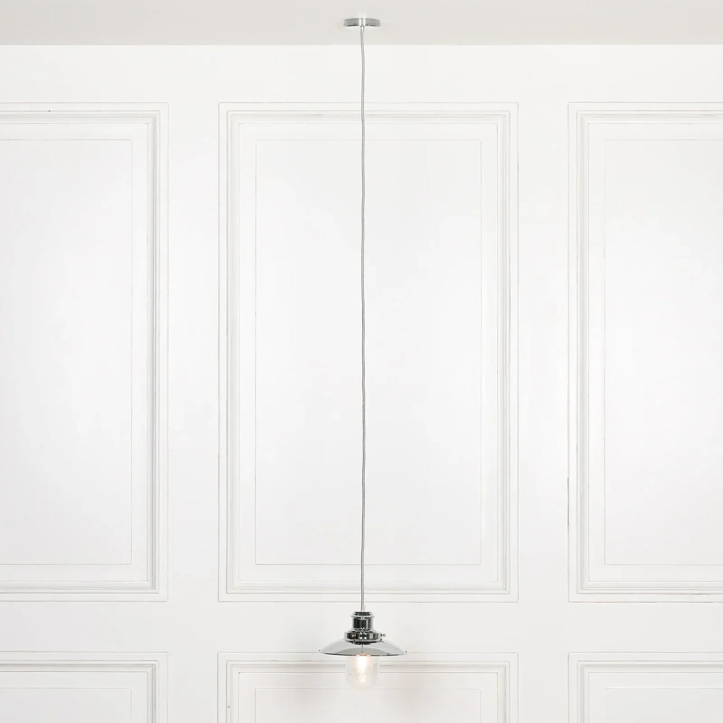 Chrome ceiling pendant light with exposed bulb against white panelled wall