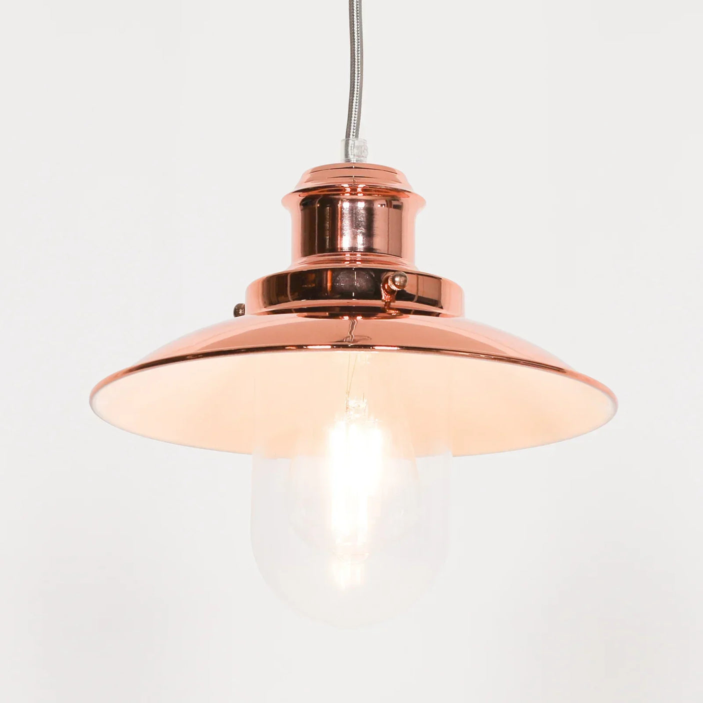 Copper pendant ceiling light with a glossy metal shade and exposed bulb, hanging against white wall