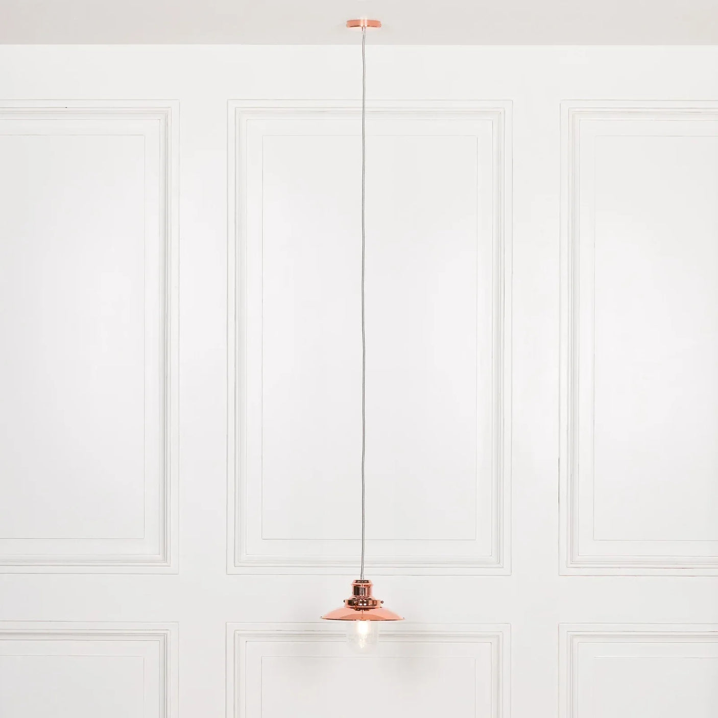 Copper pendant ceiling light with exposed bulb against white paneled wall