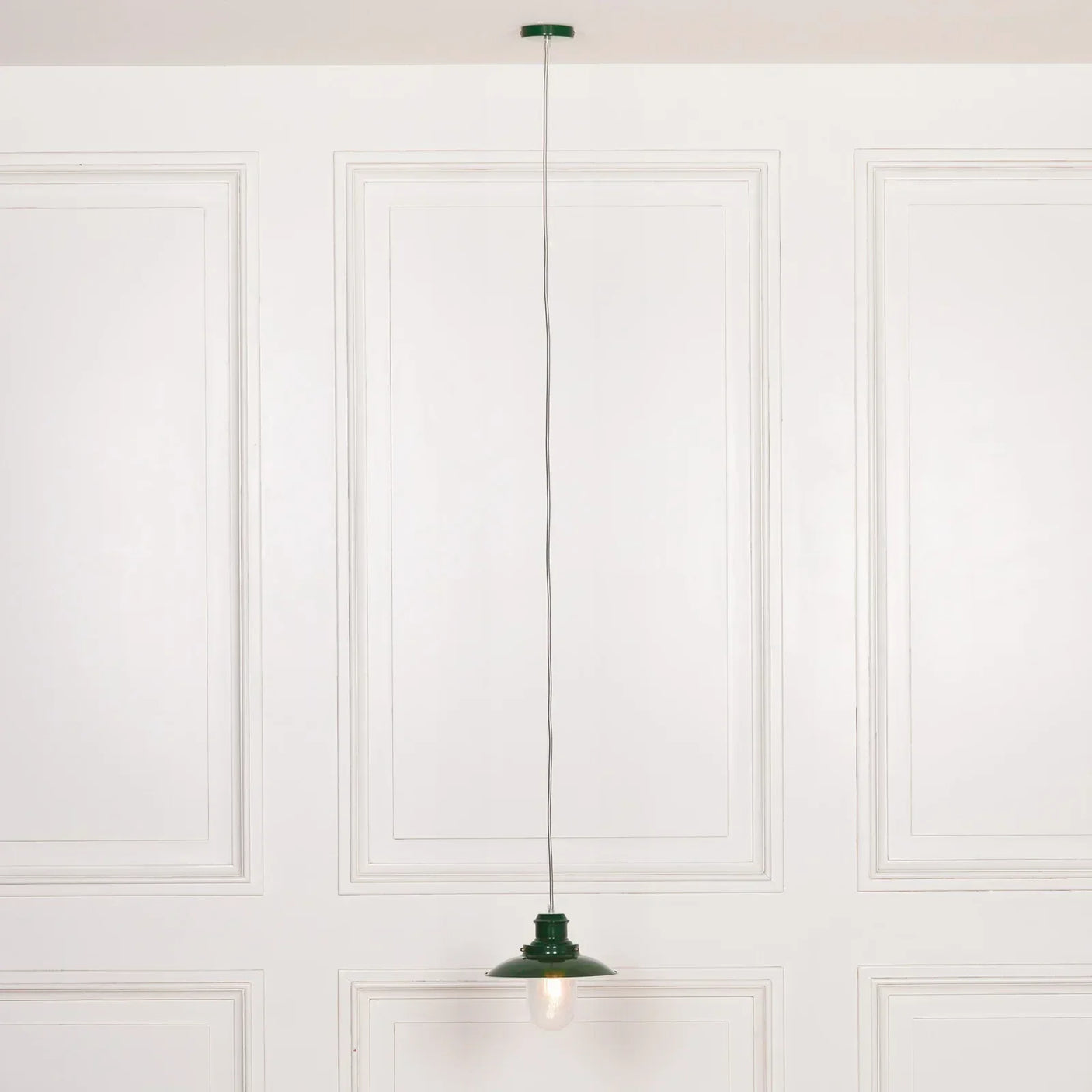 Green metal pendant ceiling light with visible bulb against white panel wall