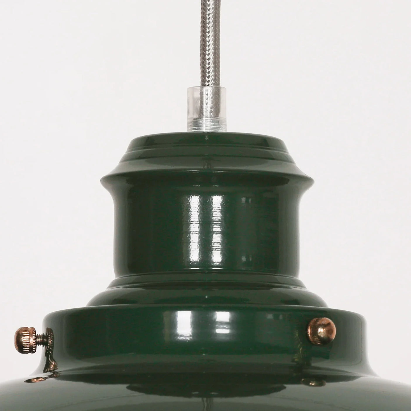 Close-up of green metal pendant light fixture with brass screw details and braided cable