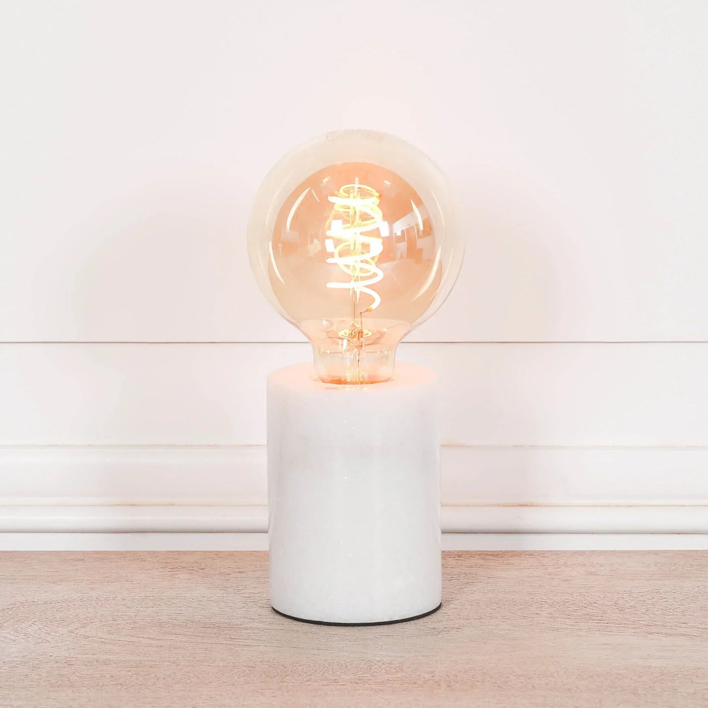 Modern table lamp with exposed bulb on white marble base on wooden surface