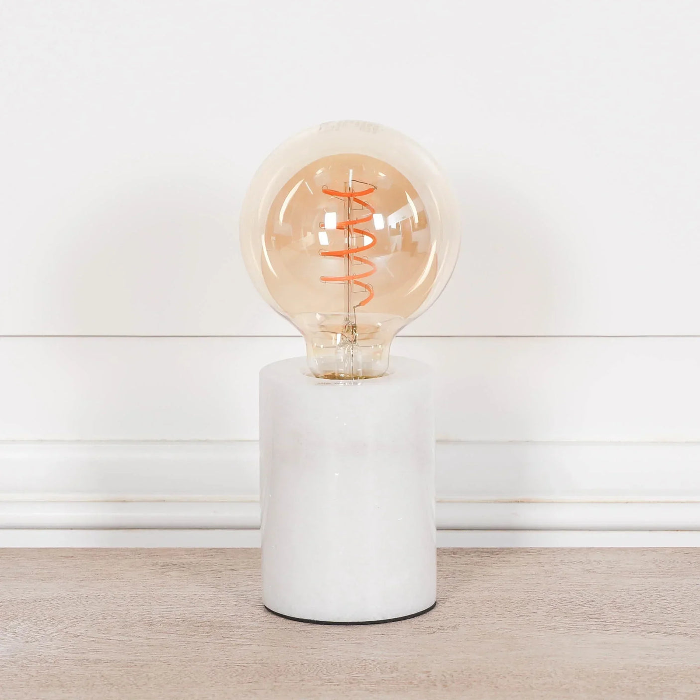 Modern marble table lamp with exposed filament bulb on wooden surface