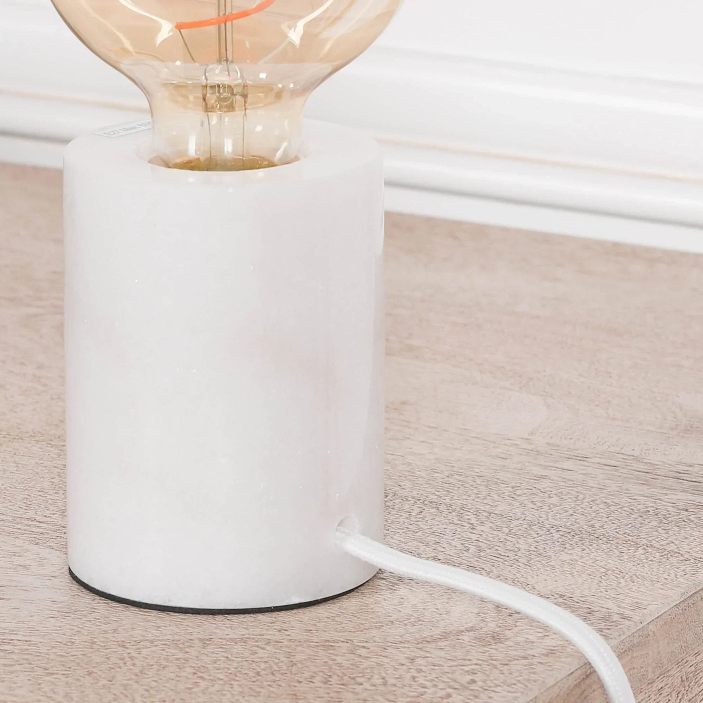 Marble base table lamp with exposed bulb on light wood surface