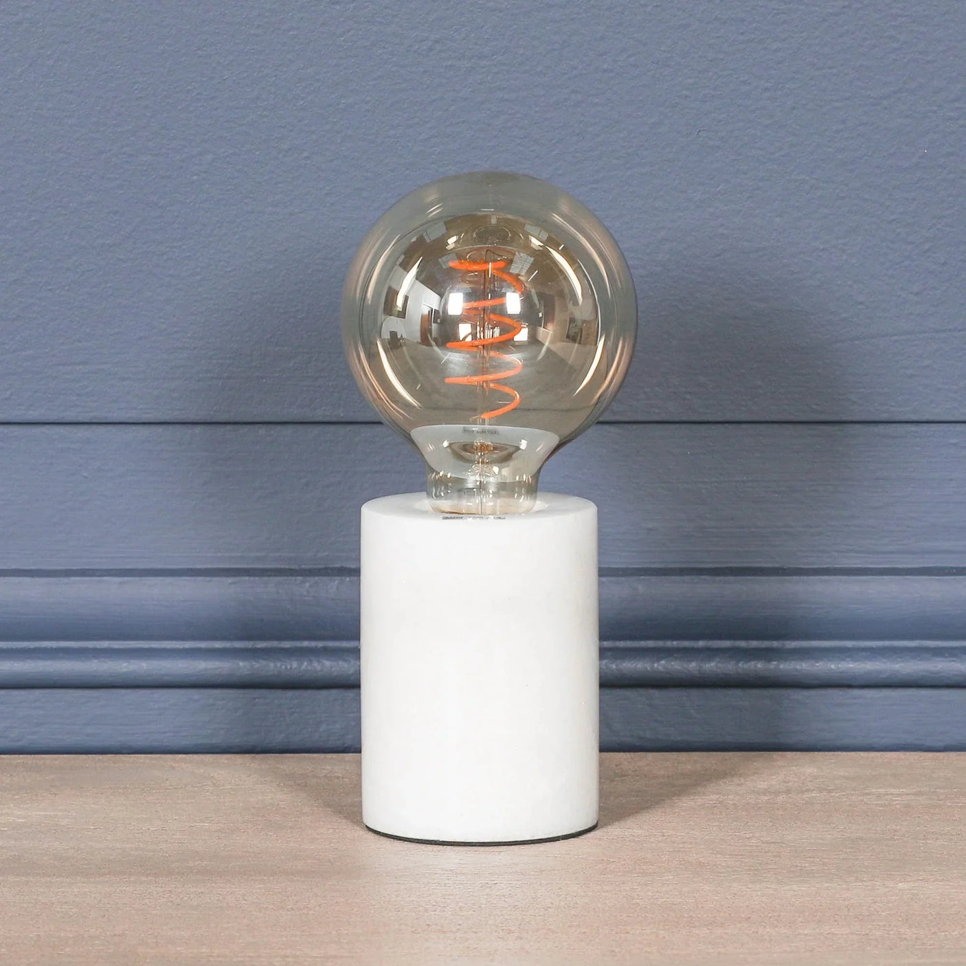 Modern table lamp with round glass bulb and white marble base on wooden surface