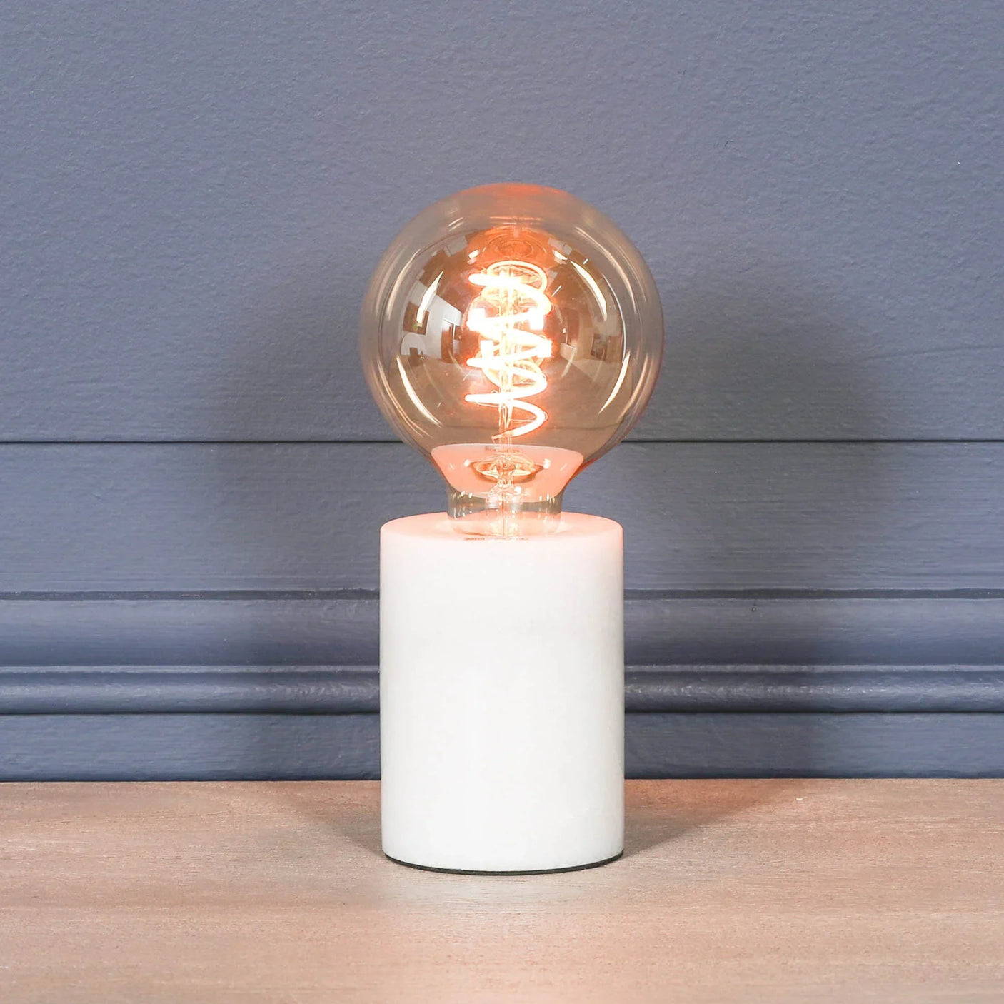 Modern table lamp with exposed filament bulb and white marble base on wooden surface