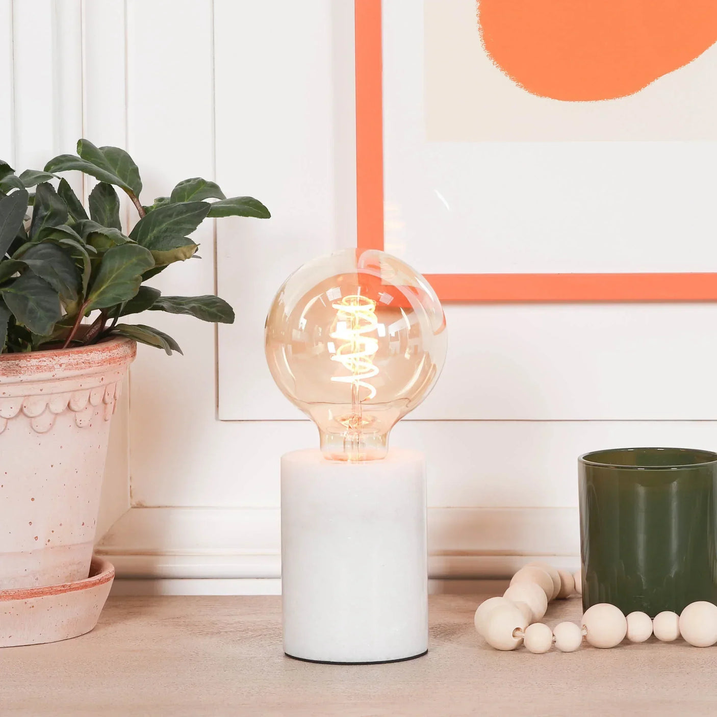 Modern table lamp with round exposed bulb and white marble base on wooden side table