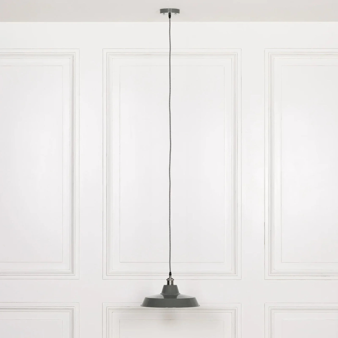 Grey metal pendant light with round shade hanging from ceiling in white panelled room