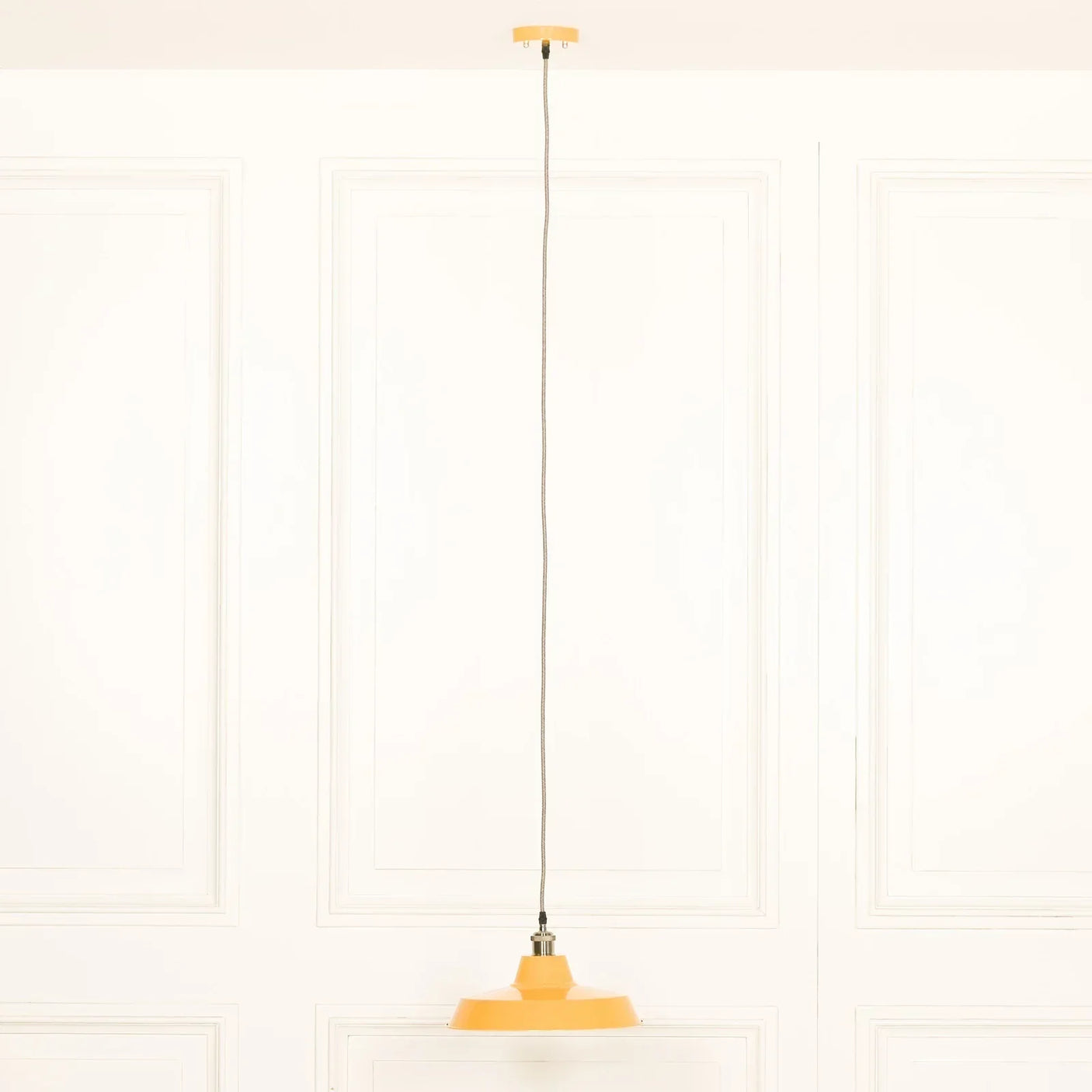 Yellow pendant ceiling light with fabric cord against white paneled background