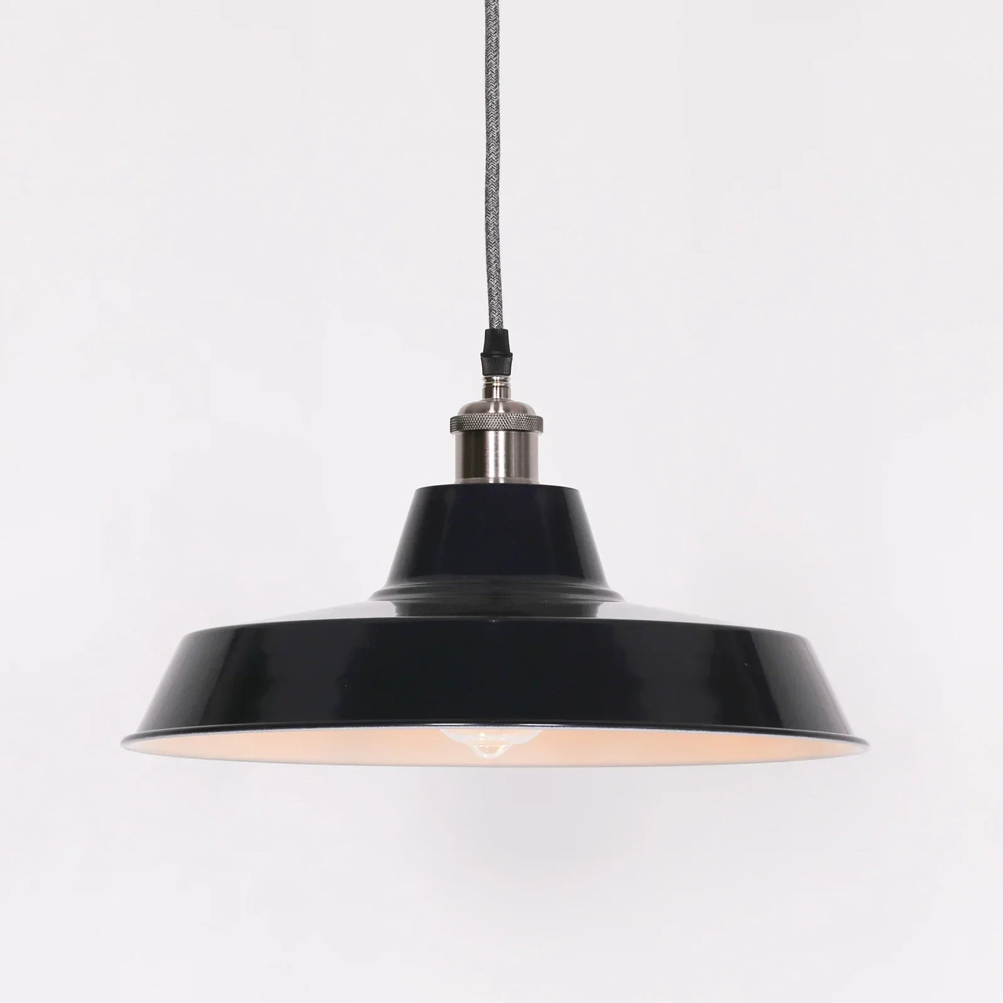 Black metal pendant light with wide shade and exposed bulb on white background