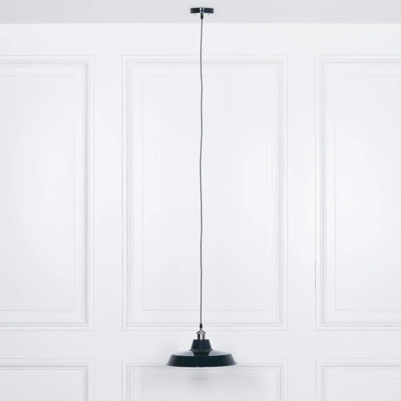 Black metal pendant ceiling light with long cord against white paneled wall