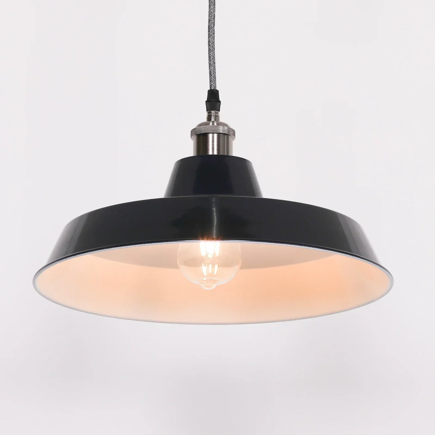 Black metal pendant light with exposed bulb and fabric cord against white background