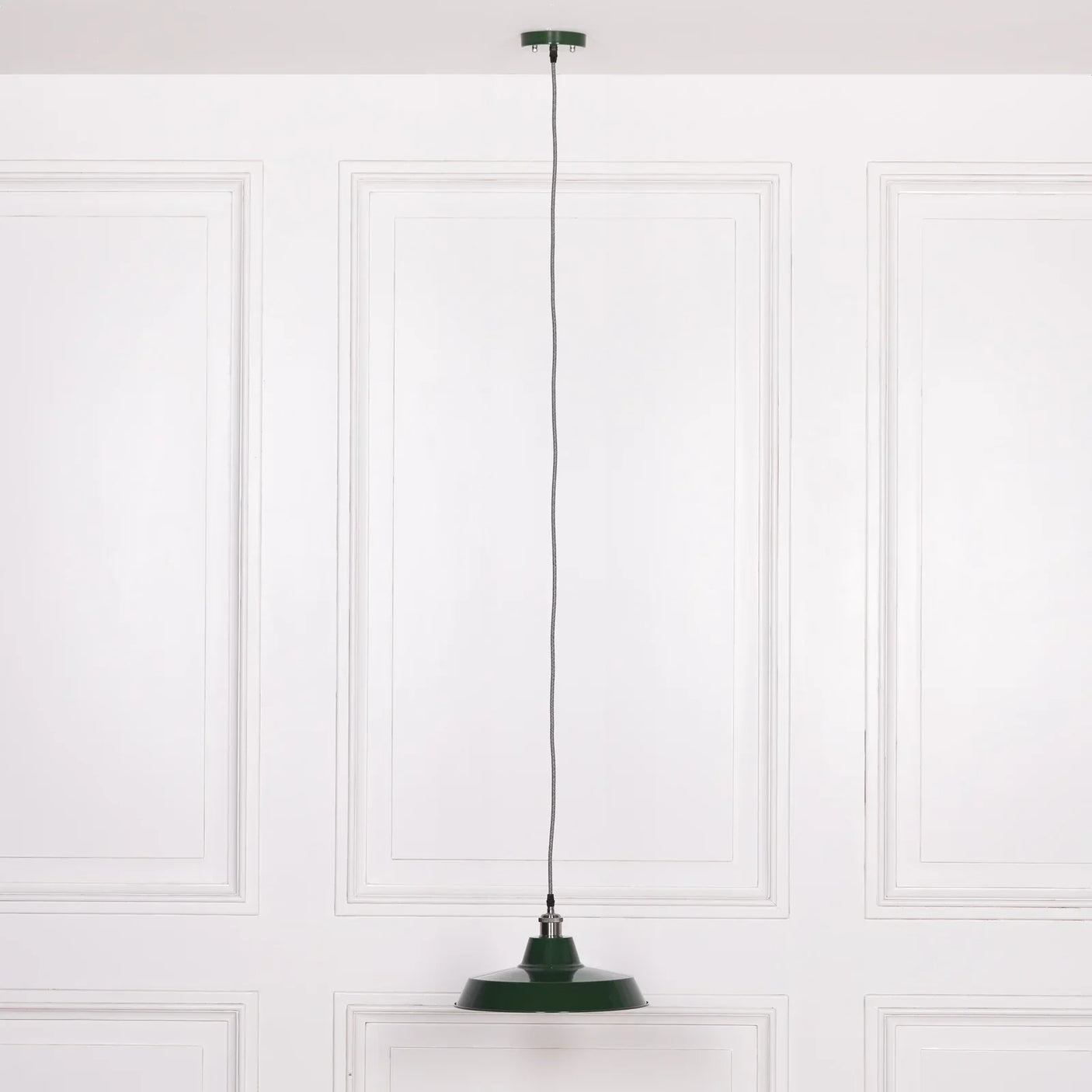 Green metal pendant light with braided cord suspended from ceiling against white panel wall