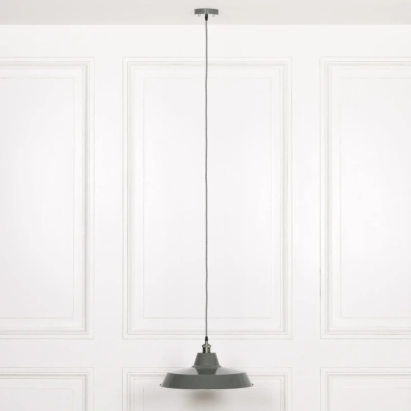 Grey metal pendant light with long cord hanging from ceiling against white panelled wall