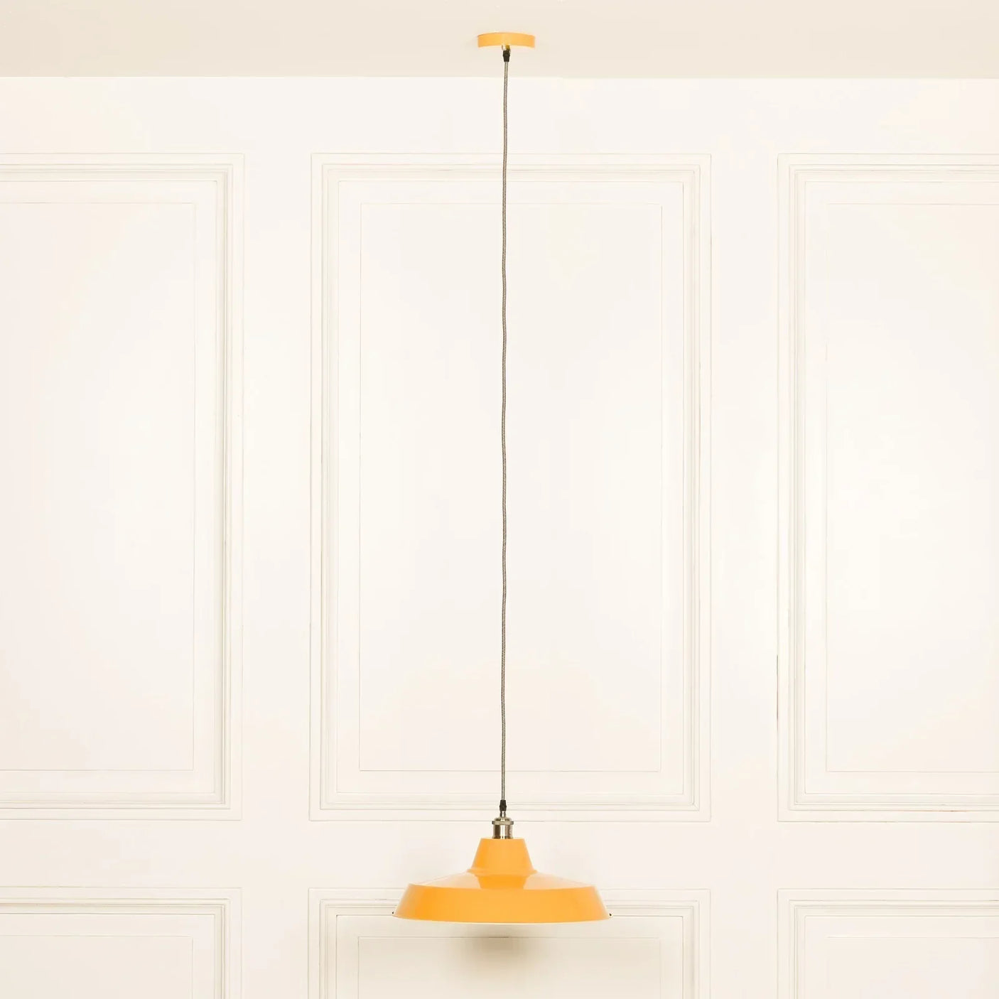 Yellow metal pendant light with long cord against white paneled wall