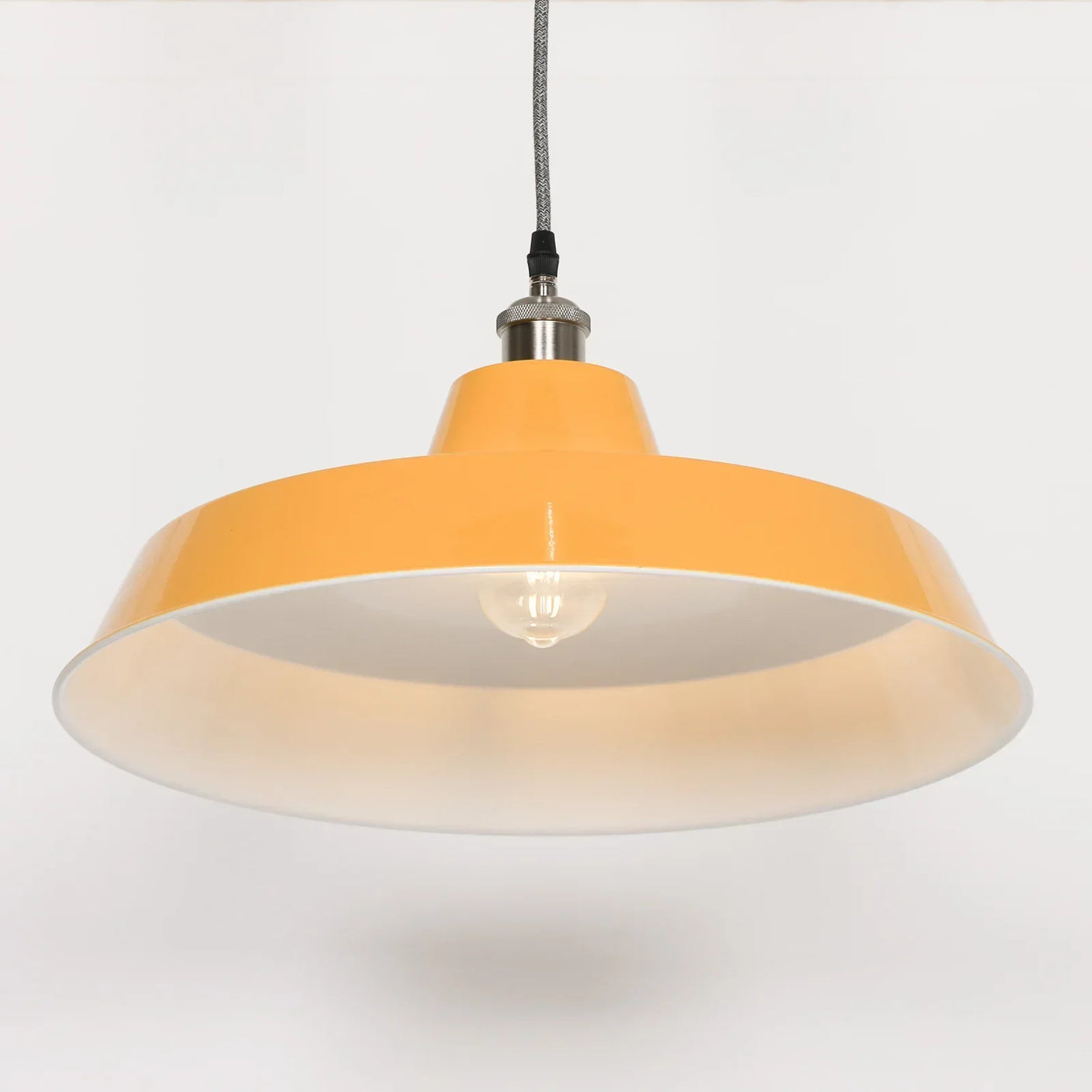 Yellow metal pendant light with exposed bulb and fabric cord, side angle view