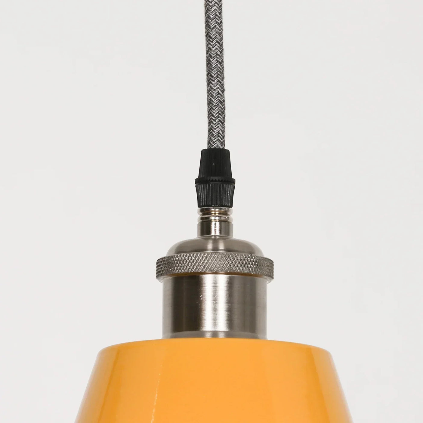 Yellow pendant light with brushed metal fixture and braided cord, close-up detail
