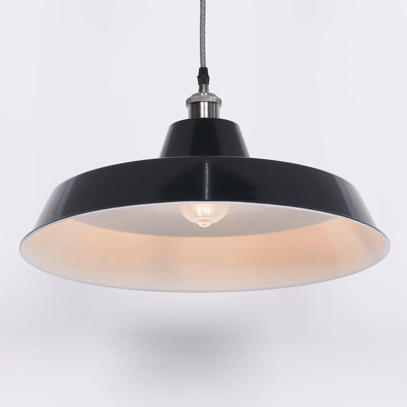 Black metal pendant light with wide dome shade and exposed bulb, hanging from braided cord