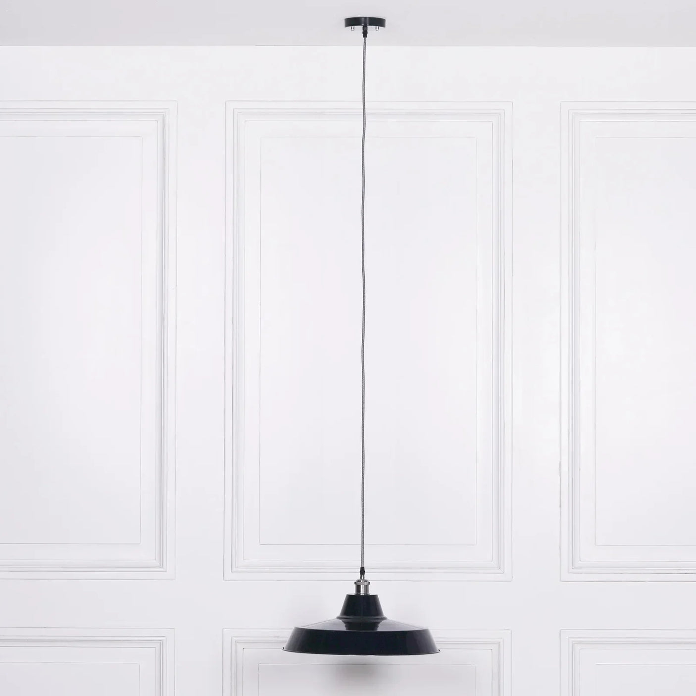 Black metal pendant light with long cord against white panelled wall