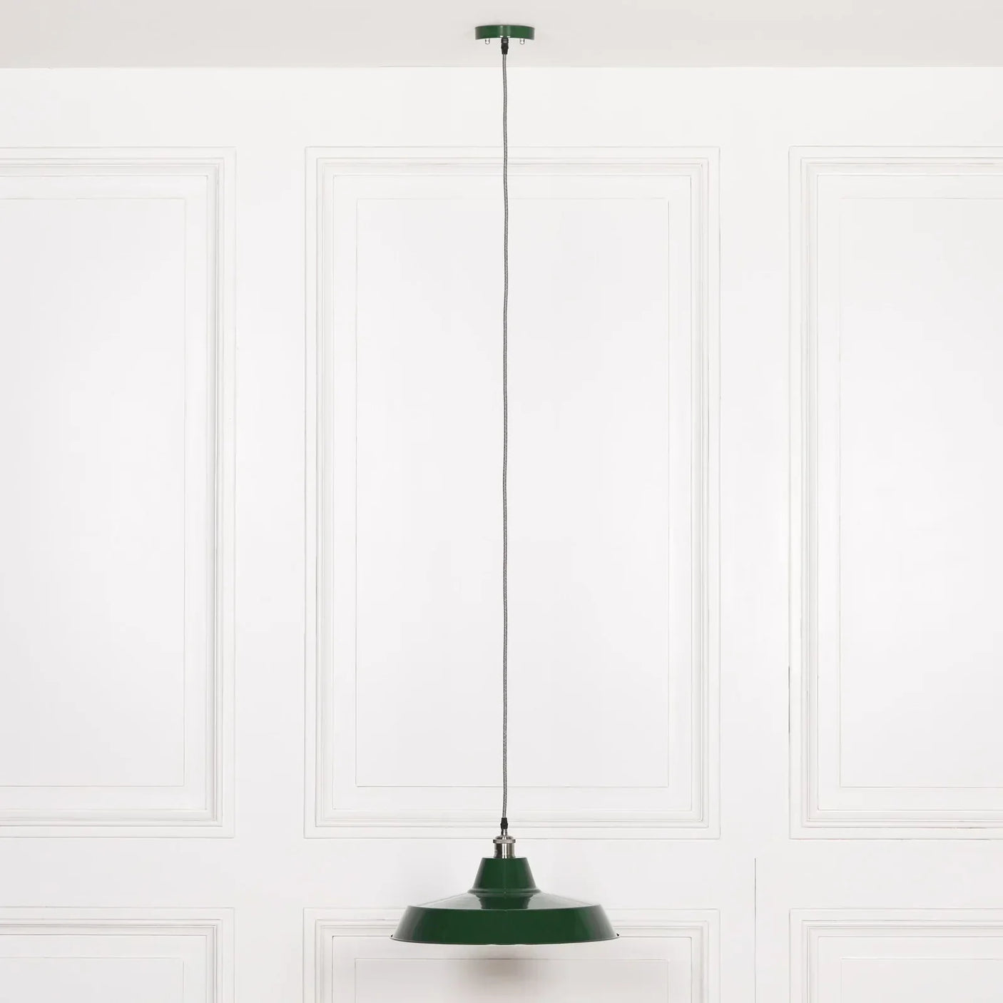 Green metal pendant light hanging from ceiling against white paneled wall