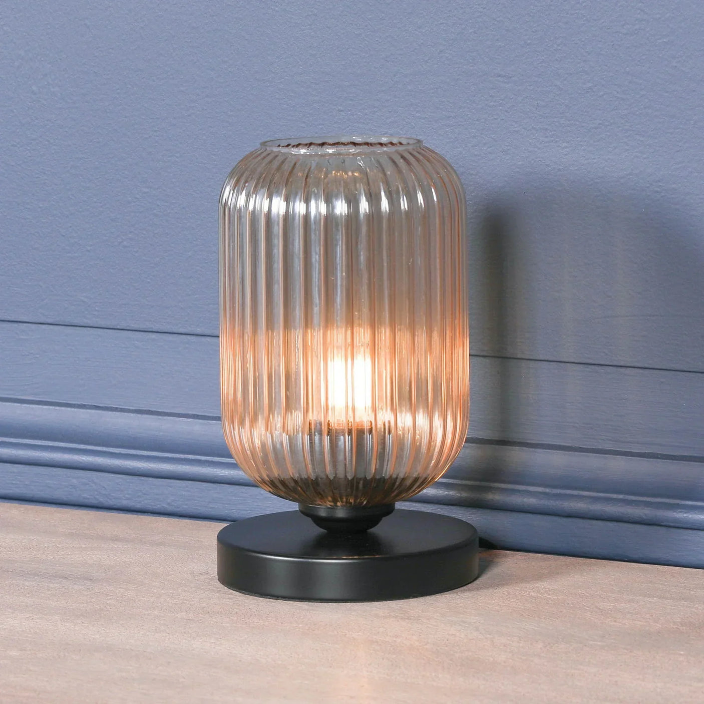 Ribbed glass table lamp with black metal base on wooden surface against blue wall