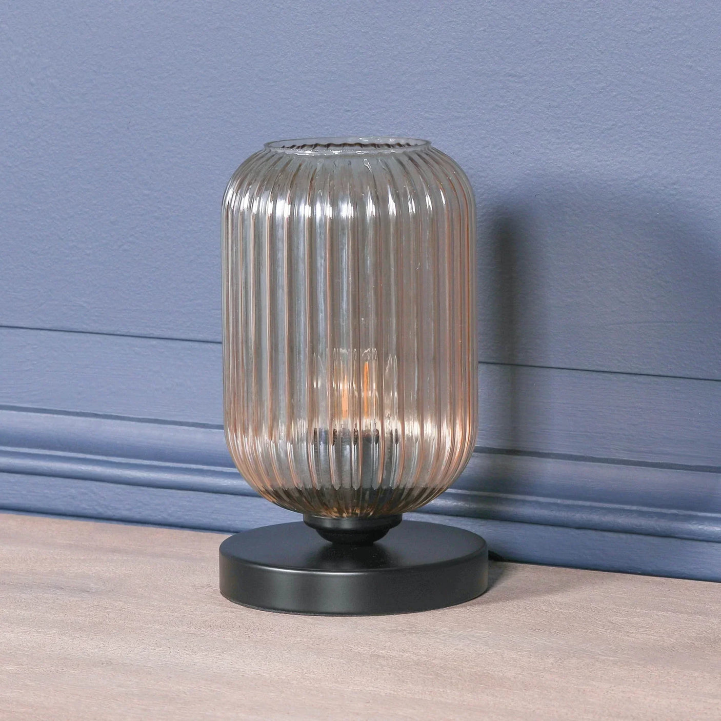 Ribbed glass table lamp with black metal base on wooden surface against blue wall