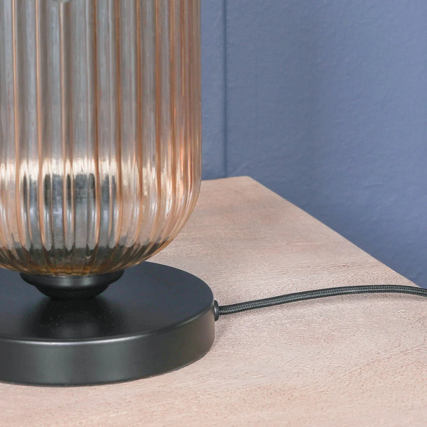 Ribbed glass table lamp with black metal base on wood surface