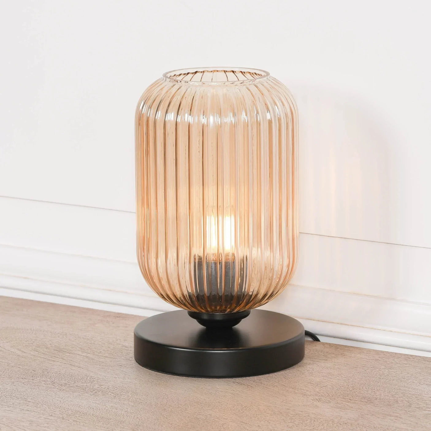 Amber glass table lamp with ribbed shade and black base on wooden floor