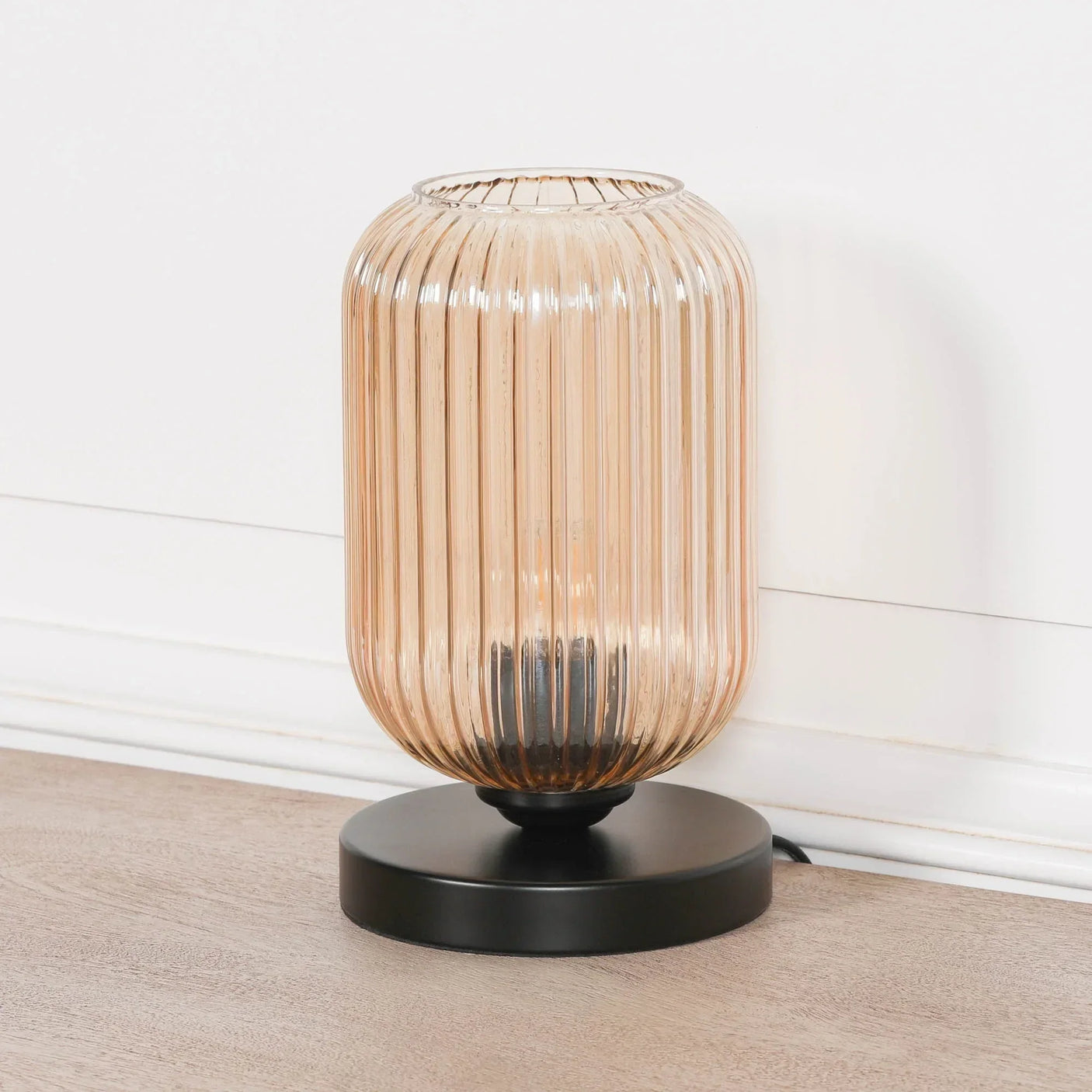 Amber ribbed glass table lamp with black base on wooden floor