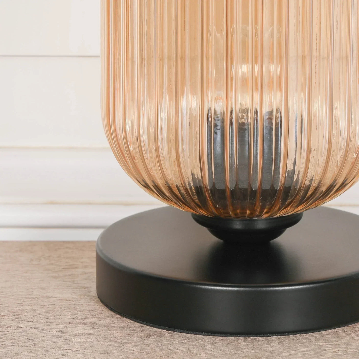 Ribbed glass table lamp with amber shade and black circular metal base on wood surface